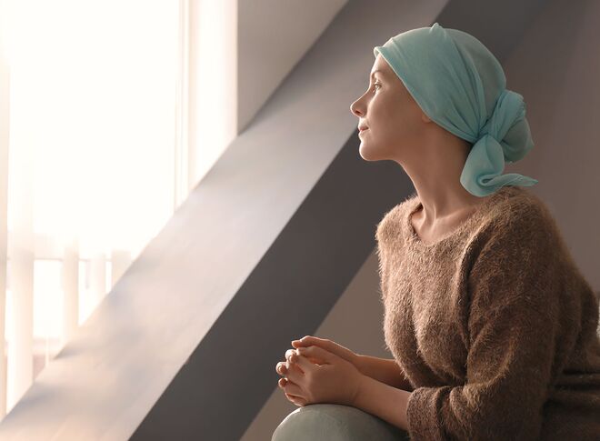 Cancer patient with a turquoise headdress looks out of the window